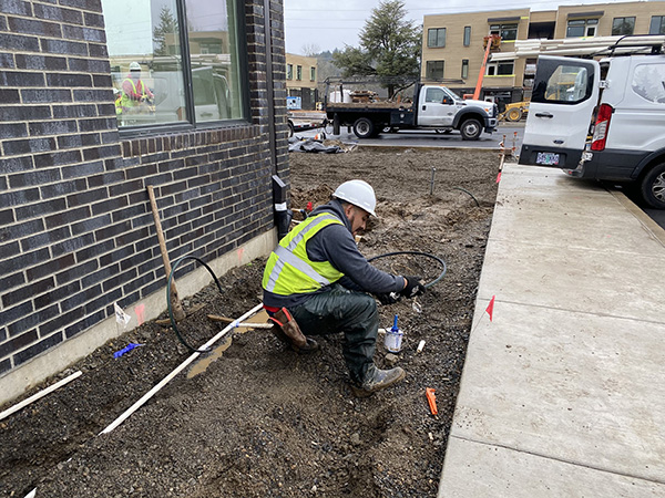 man with hardhat working on irrigation tubing outside a commercial building